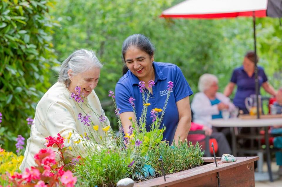 Two women planting flowers in a planter on the patio.